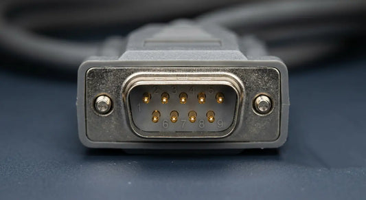 A macro photo of a male DB9 connector, with extremely shallow depth of field, focusing on the nine gold-plated pins and their tiny molded numeric labels, suitable for a technical blog header.
