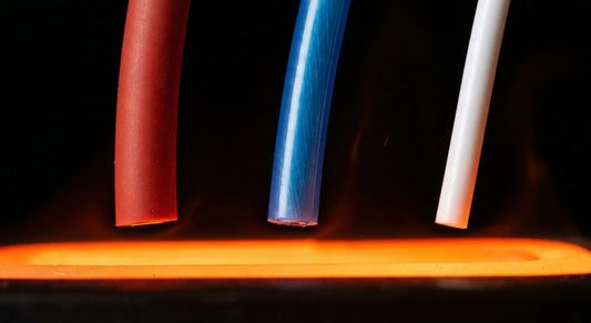 A dramatic macro photograph of Silicone, FEP, and PTFE insulated wires suspended over a glowing orange heating element, demonstrating their resistance to extreme thermal stress.